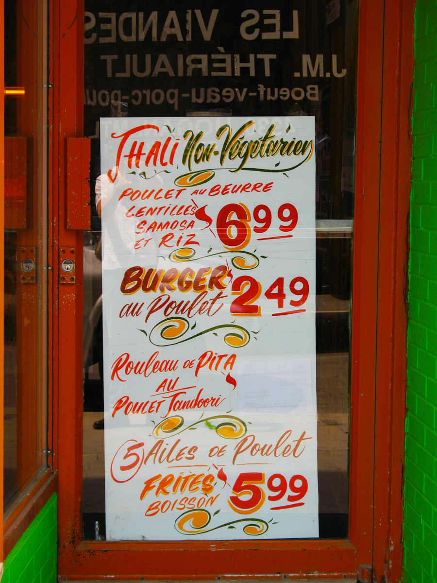 photo of a doorway with a sandwich board promoting thali, burgers, pita sandwiches, and chicken wings in French