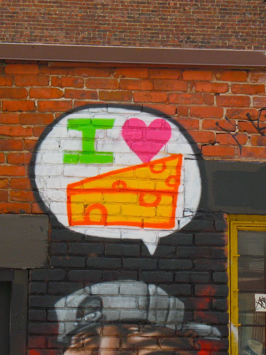 photograph of urban graffiti on a city wall showing a thought bubble saying "I love cheese" in graphic elements