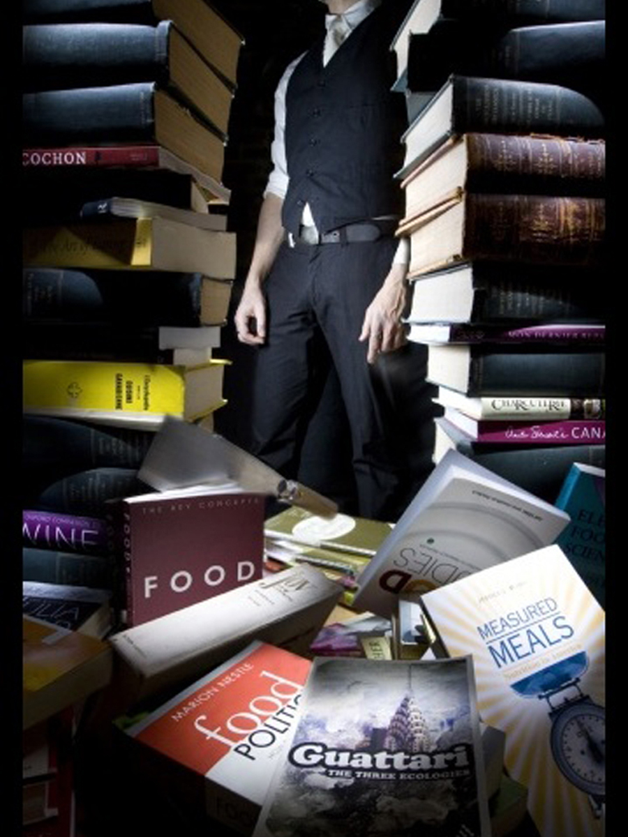 photo of a figure standing behind a pile of food books, one of which has a cleaver in it